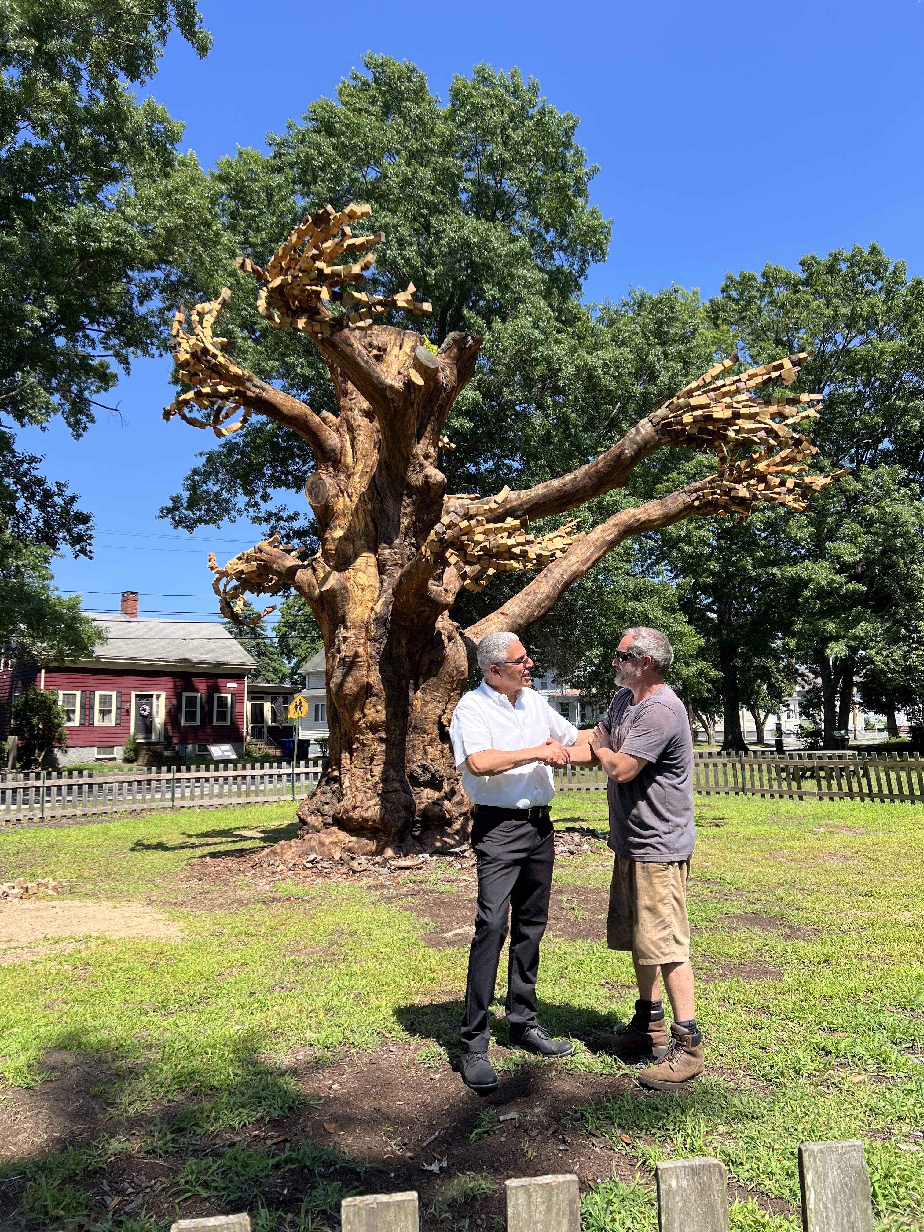 Mayor DaSilva shaking sculptor's hand in front of the tree